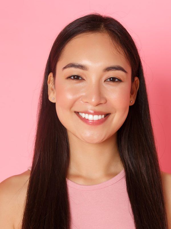 Beauty, fashion and lifestyle concept. Close-up of beautiful happy asian girl with perfect white smile, looking upbeat, standing hopeful and upbeat over pink background. Copy space